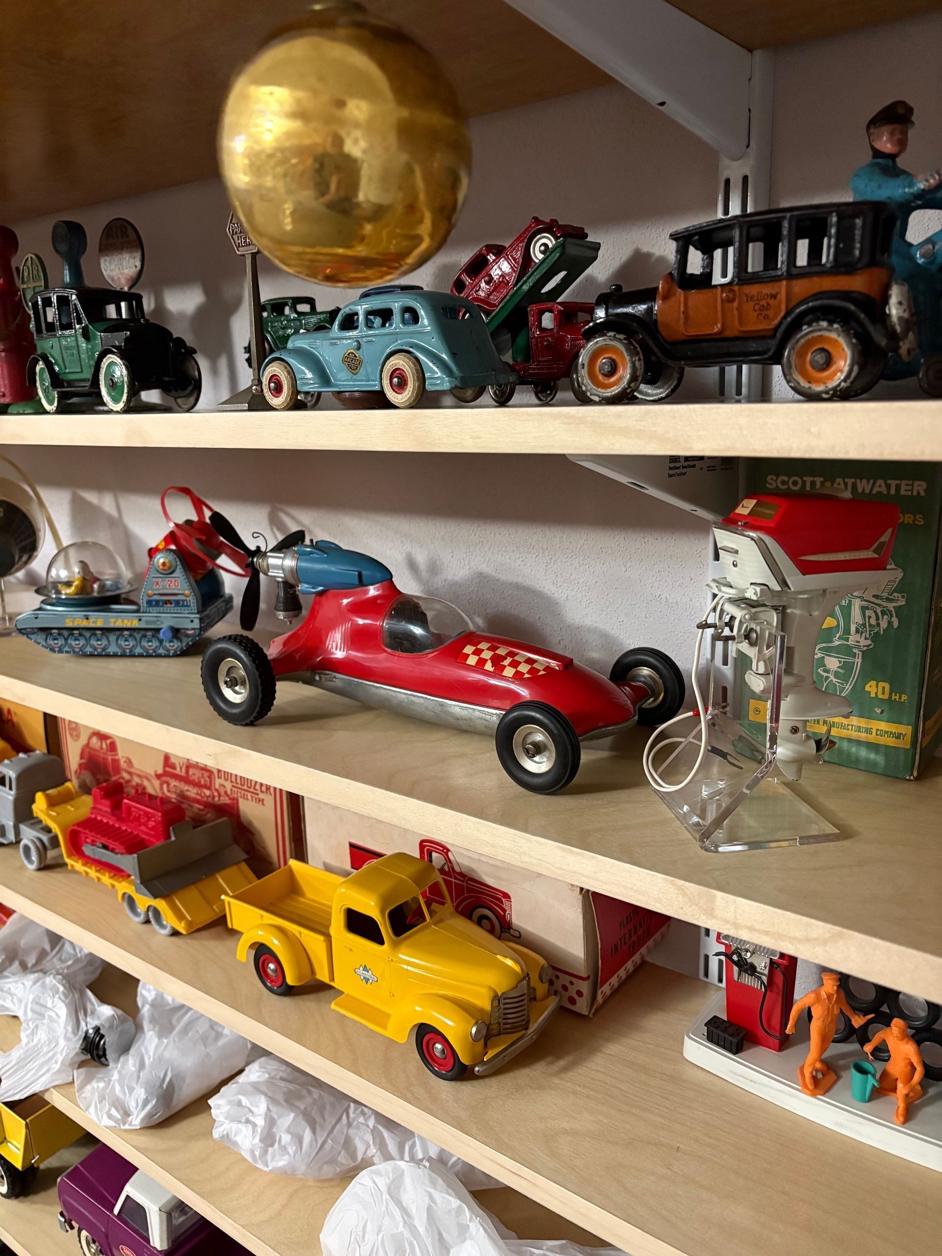 Shelf of colorful toy cars and trucks, including red and yellow models and a gold ball on the top shelf.