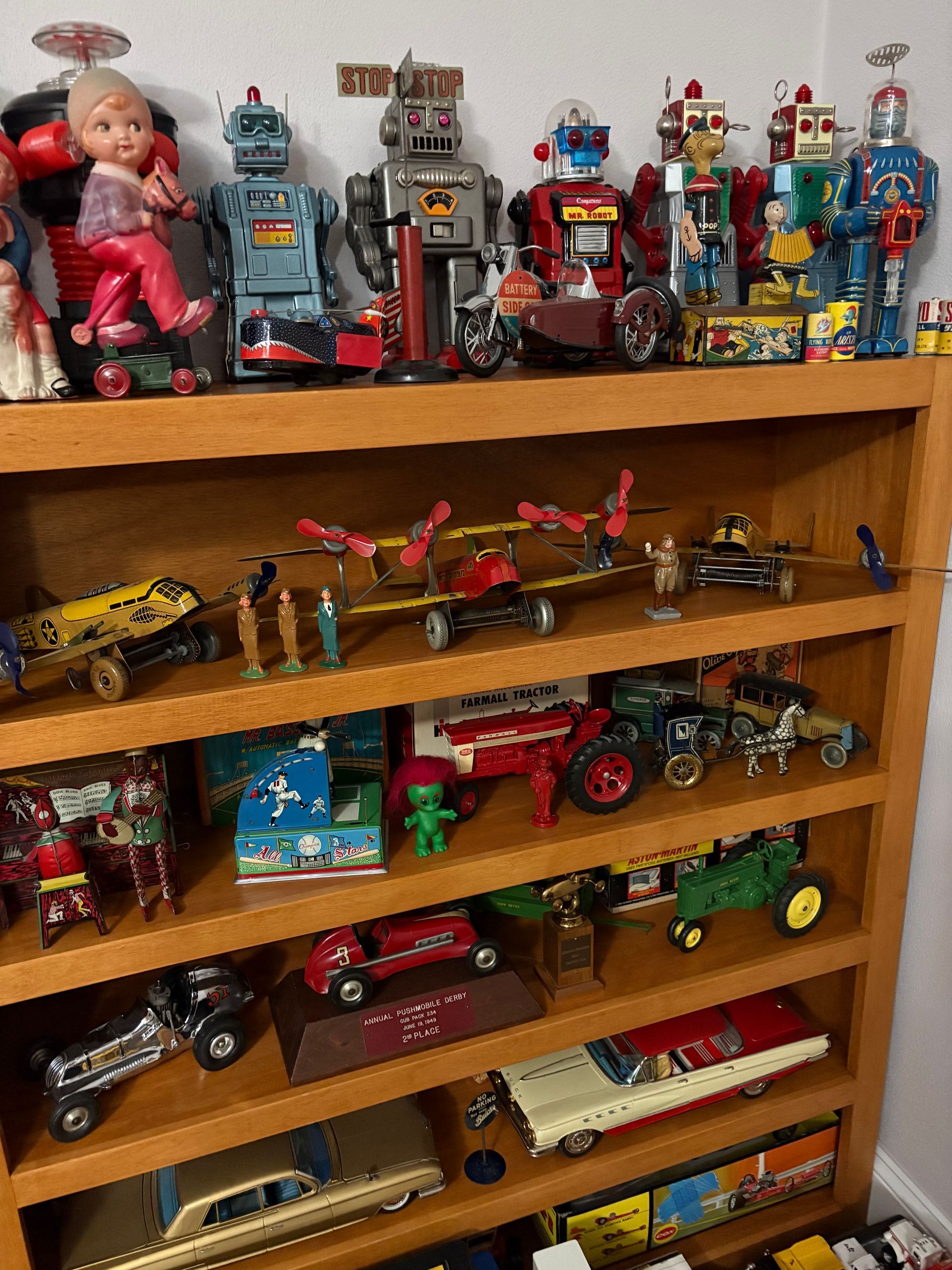 Wooden shelf filled with vintage toy cars, robots, and dolls arranged on multiple shelves