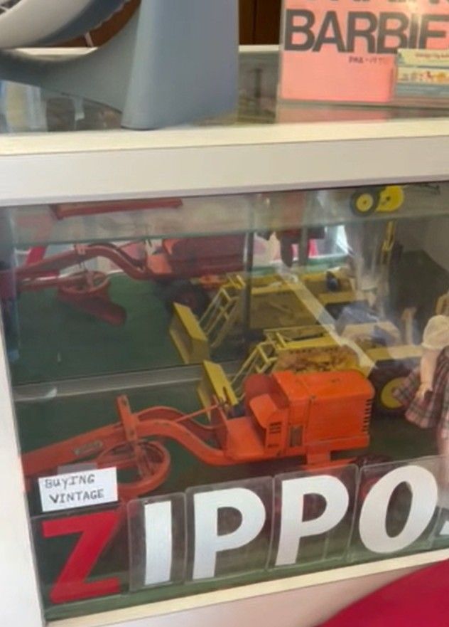 Display of vintage Zippo lighters in a glass case with large white ZIPPO lettering and toy trucks on top