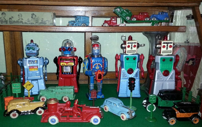 Vintage toy display on wooden shelves featuring multiple tin robots, antique cars, and a red fire truck.