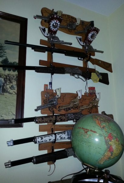 A wall display of several rifles and pistols mounted on wooden plaques, with a globe placed in the foreground.