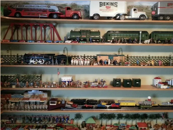 A collection of vintage model trains, trucks, and miniature figures displayed on multiple wall-mounted shelves.
