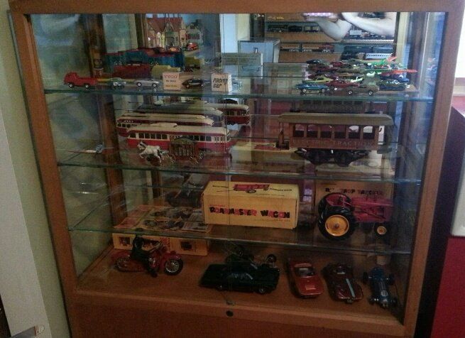 A wooden display case filled with various vintage toy vehicles, including model cars, a tractor, and a trolley.