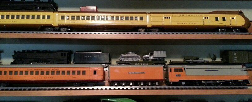 Two shelves displaying vintage toy train cars and engines in yellow, orange, and black, lined up on tracks.