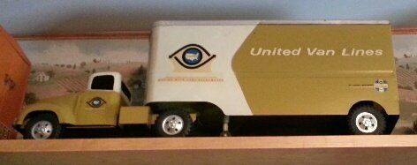 A United Van Lines toy semi-truck with a yellow cab and white and yellow trailer sitting on a wooden shelf.