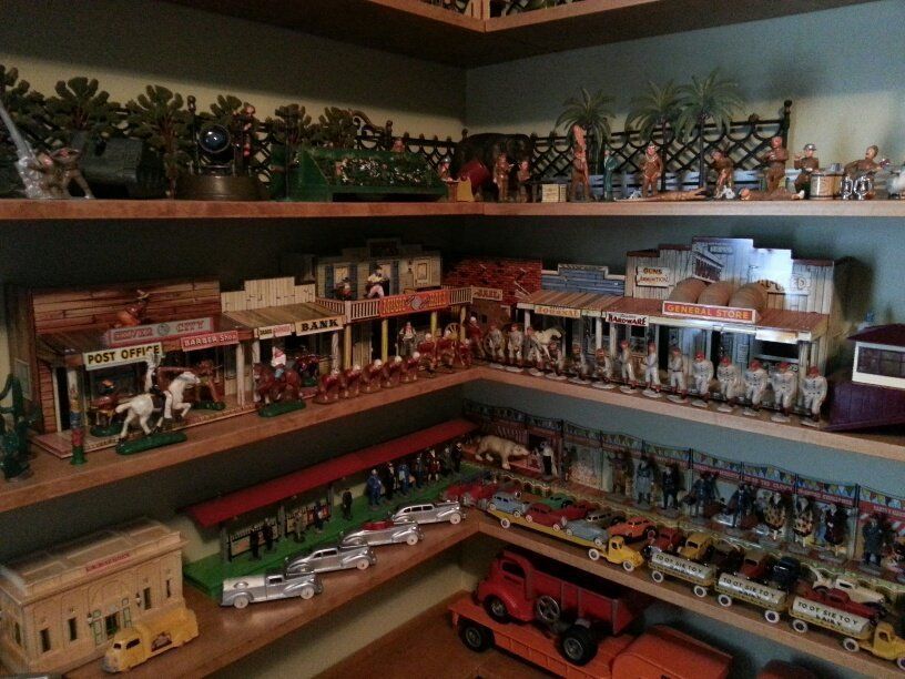 Wooden shelves filled with a collection of vintage Western town model buildings, toy soldiers, horses, and model cars.