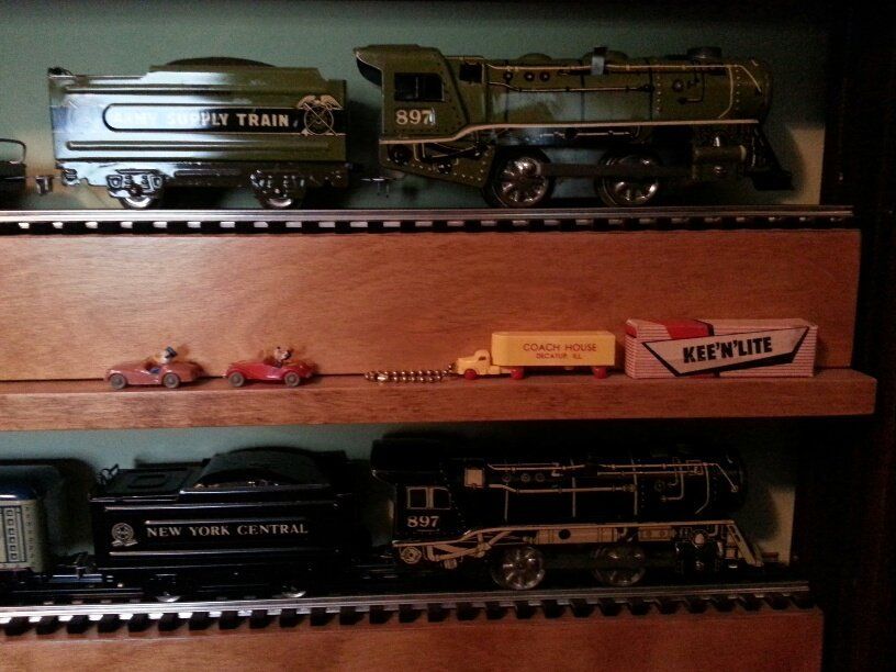 Vintage toy steam locomotives and smaller toy cars displayed on three wooden shelves.