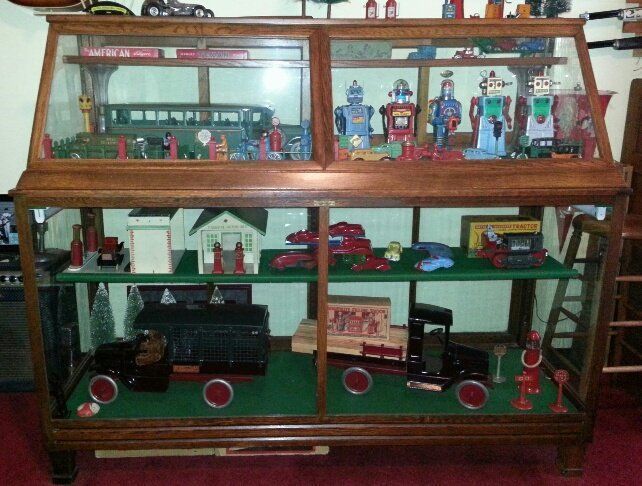 An antique wooden display case filled with a collection of vintage toy robots, model vehicles, and buildings.