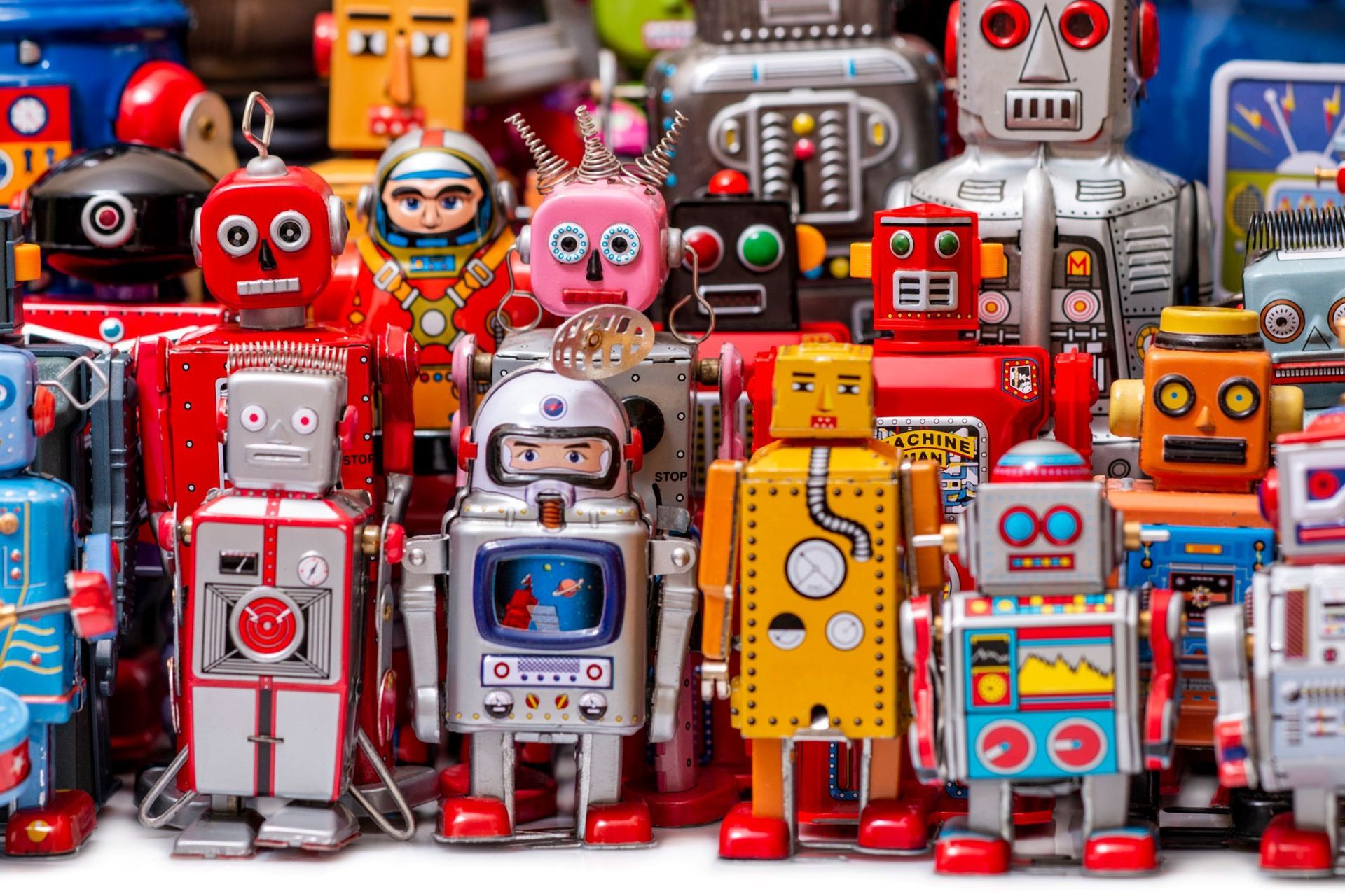A large collection of vintage-style tin toy robots in various colors, designs, and expressions crowded together.