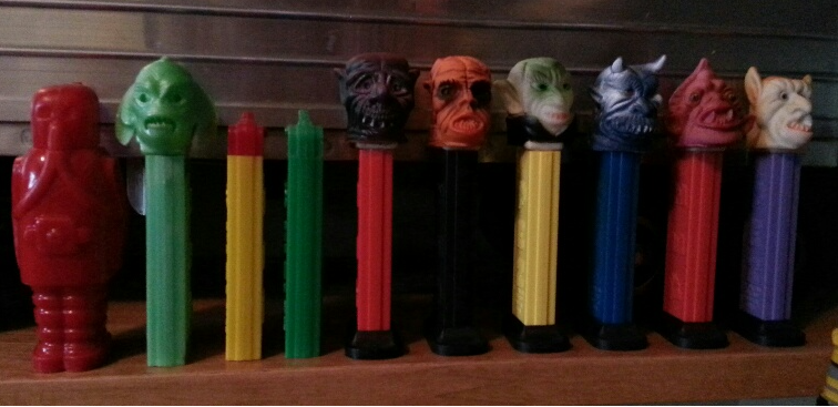A line of various collectible PEZ dispensers, including alien and monster characters, displayed on a wooden surface.