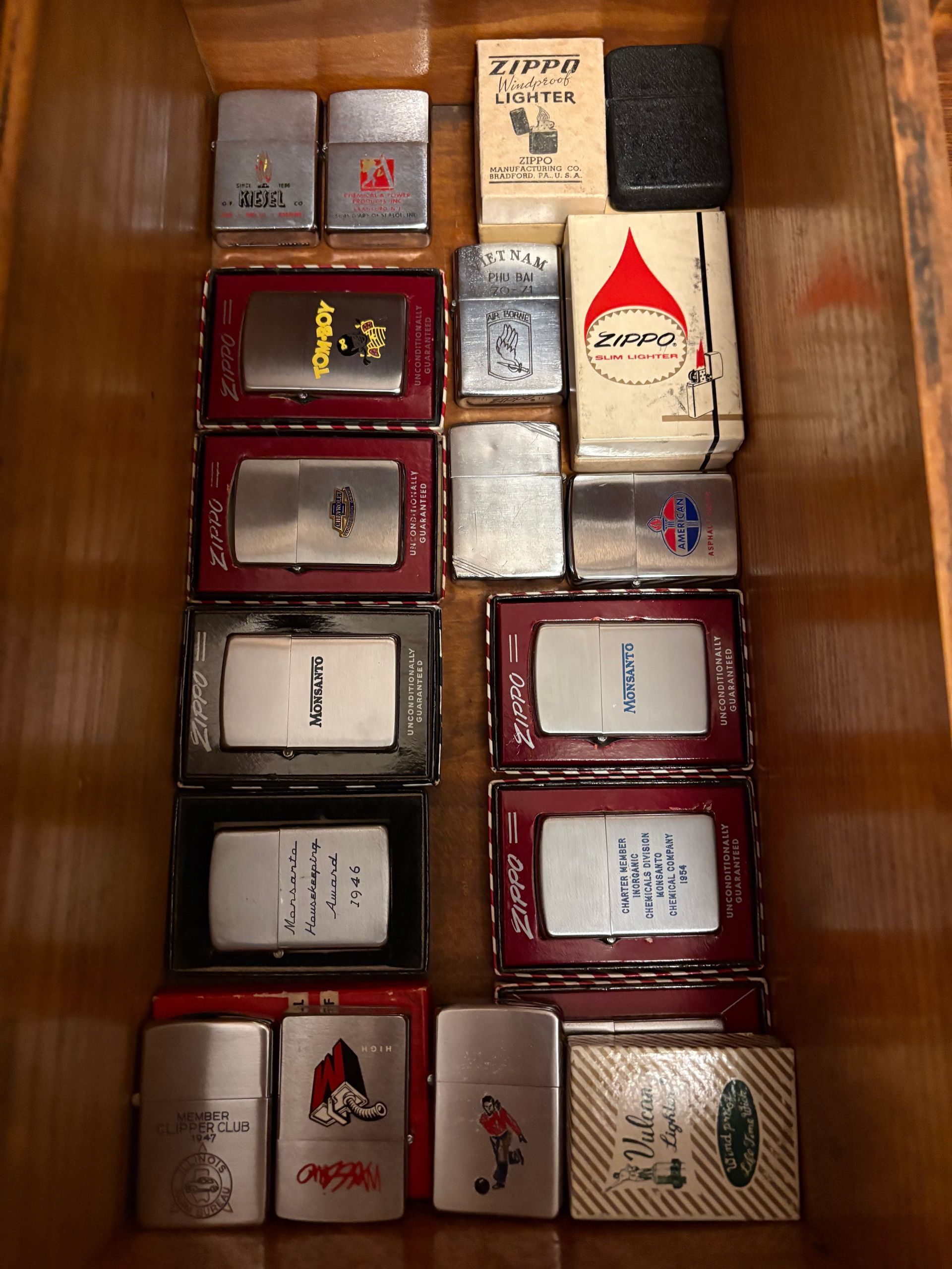 Assorted packaged Zippo lighters in a wooden display case.