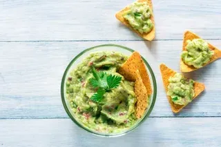 Guacamole in a bowl, served with tortilla chips on a white, weathered wood table.