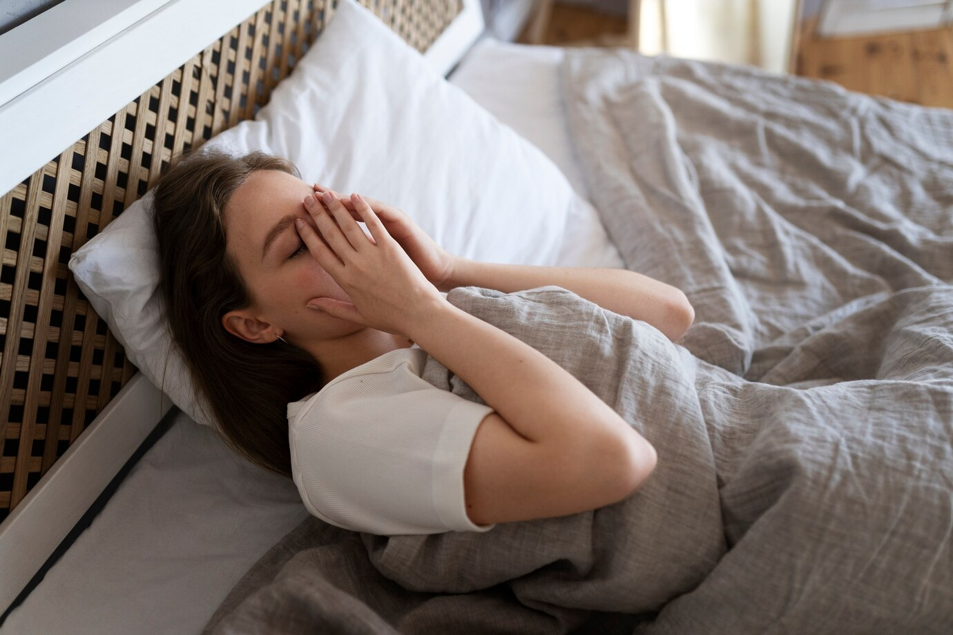 Woman in bed, covering face with hands, appearing distressed.