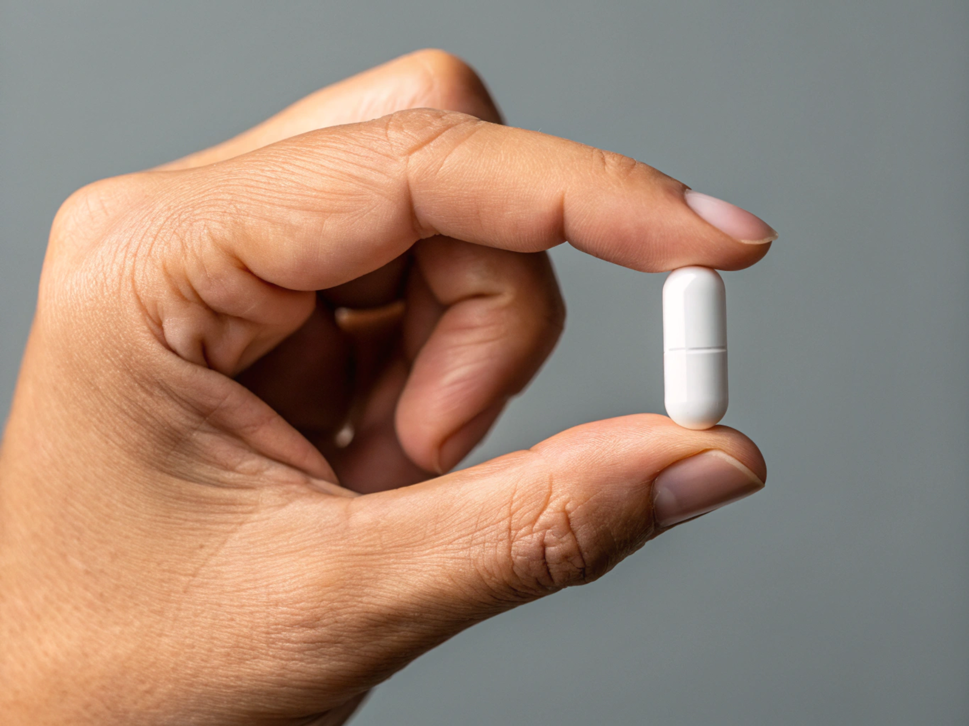 Hand holding a white capsule-shaped pill between thumb and forefinger.