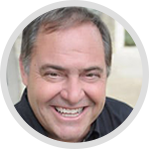 Man with short dark hair, smiling broadly with white teeth, in front of a neutral background.