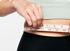 Person measuring their waist with a tape measure; the person is wearing a sports bra and leggings.