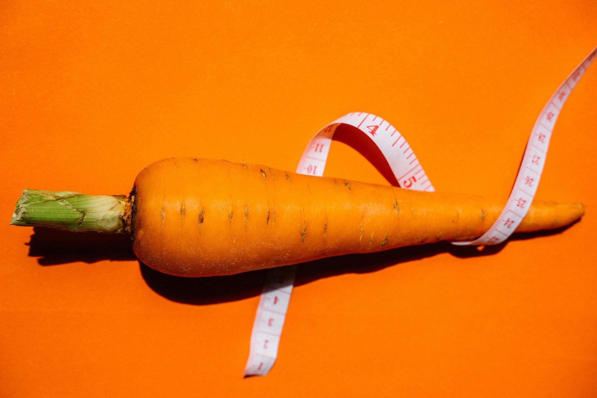 Carrot wrapped with a white measuring tape on an orange background.