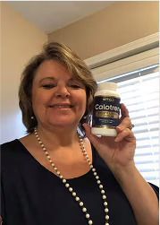 Woman holding a bottle of "Calotren" supplement; smiling, indoor setting, pearl necklace, dark top.
