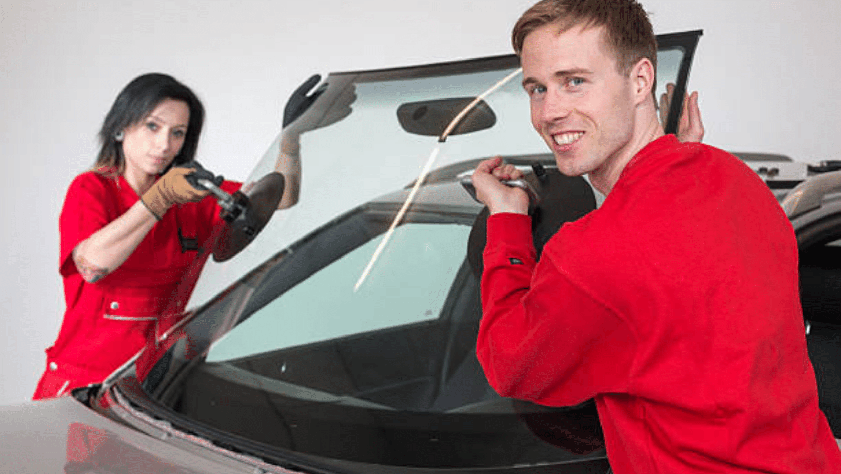 A man and a woman are installing a windshield on a car.