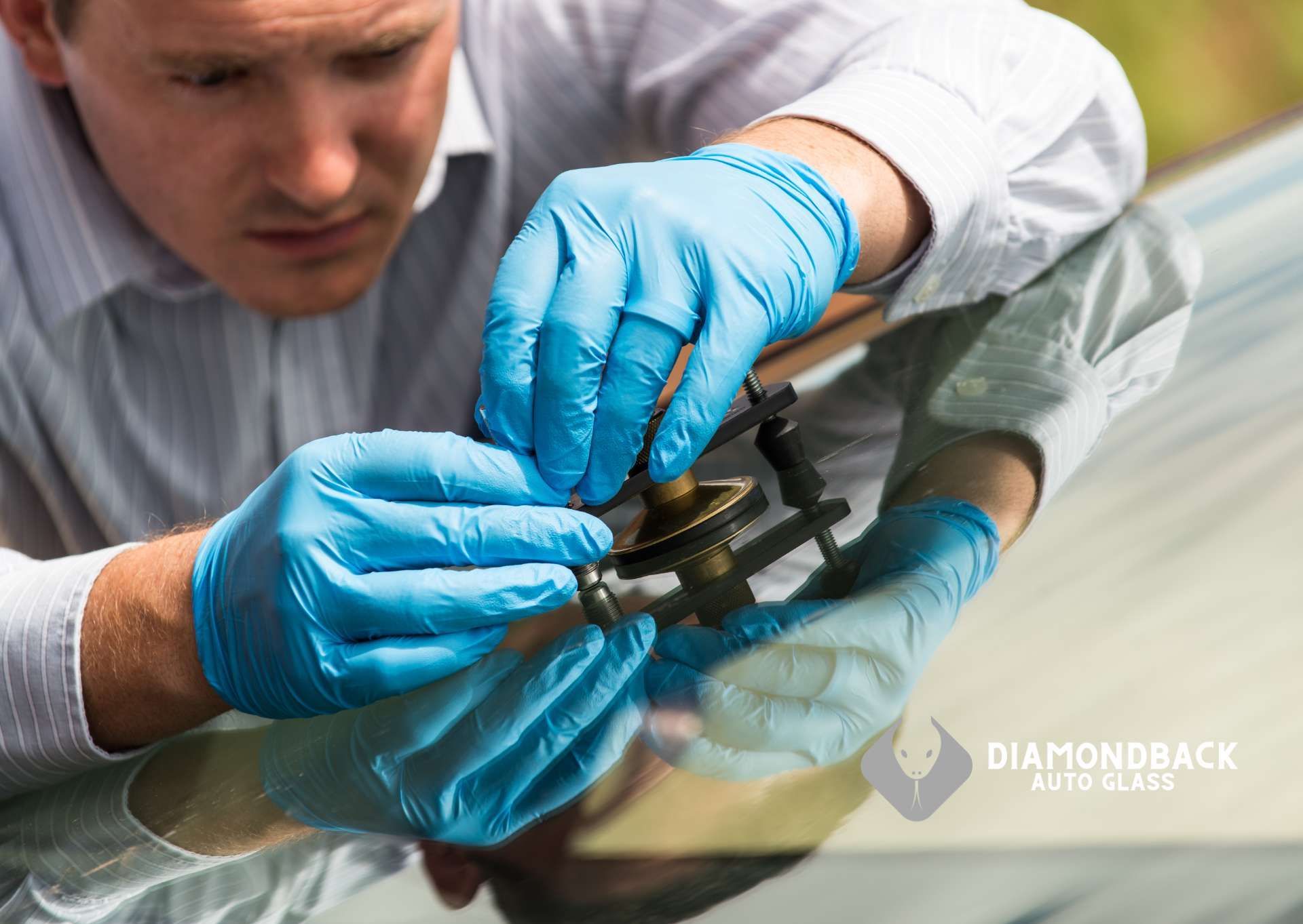 A man wearing blue gloves is repairing a cracked windshield on a car.