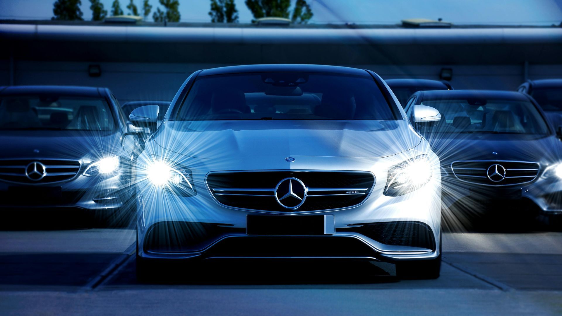 A row of mercedes benz cars are parked in a parking lot at night.