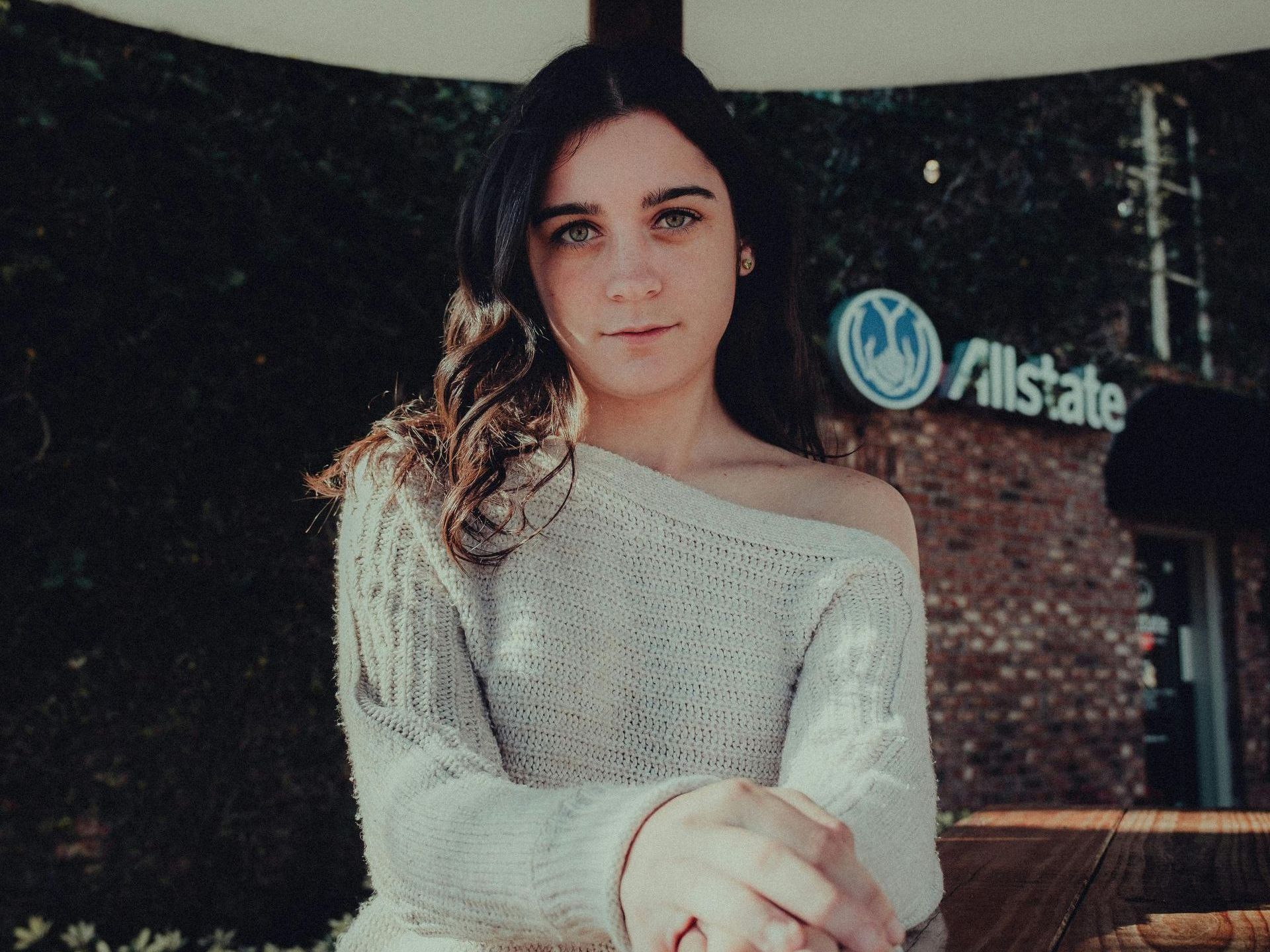 A woman in a sweater is standing in front of an allstate building