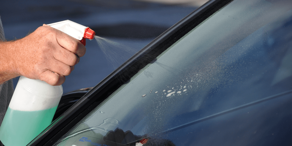 A man is cleaning the windshield of a car with a spray bottle.