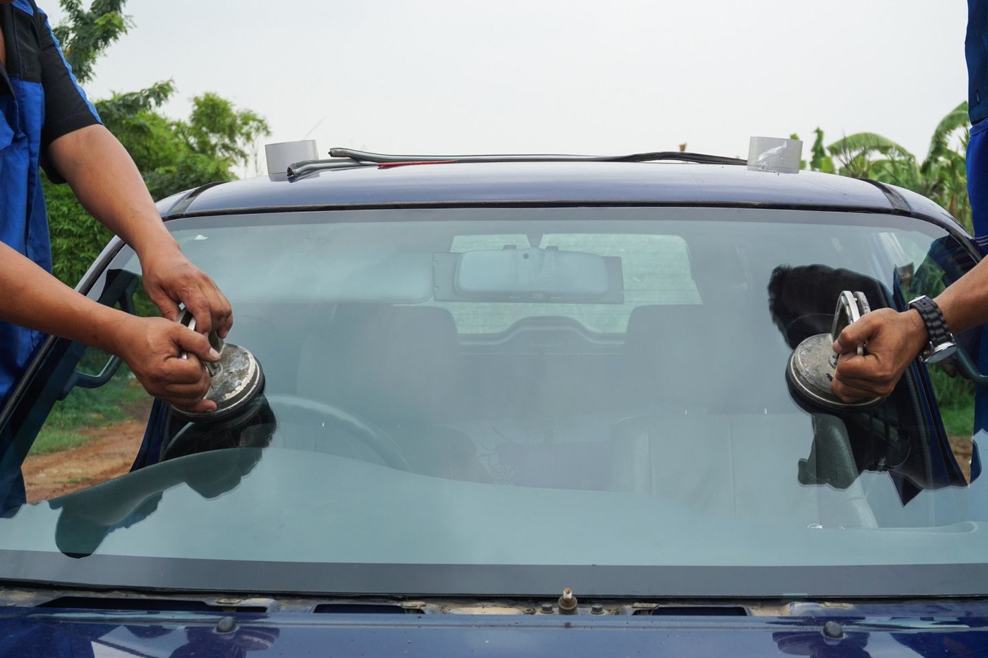 Two men are installing a windshield on a blue car.