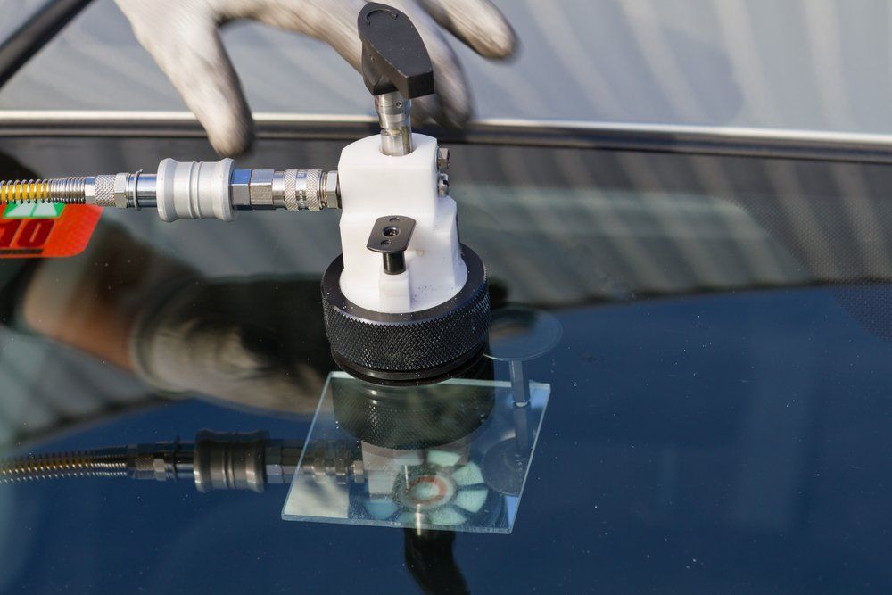 A person is repairing a windshield on a car with a tool.