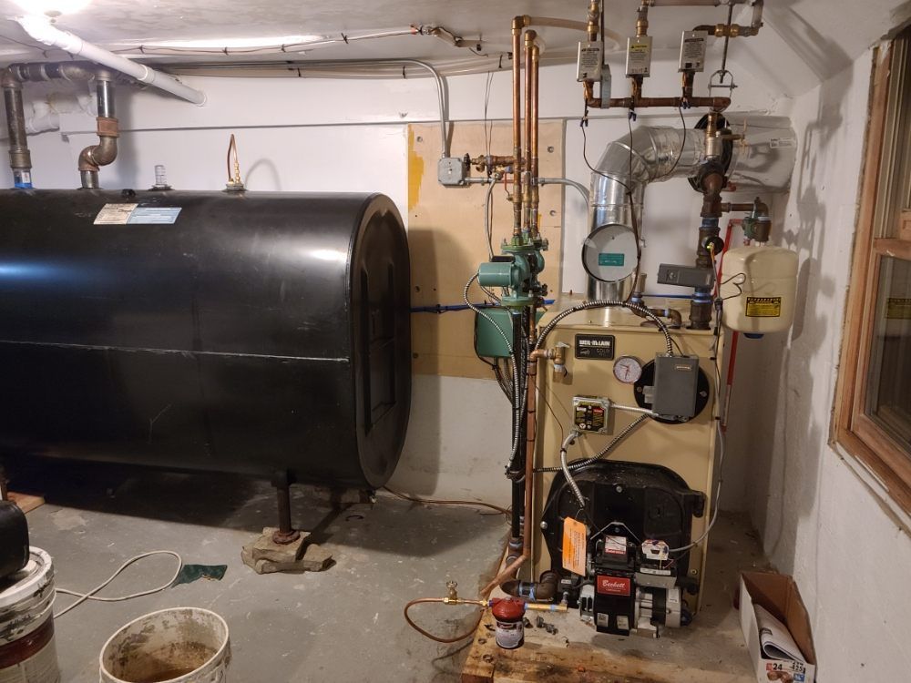 A boiler is sitting in a basement next to a black tank.