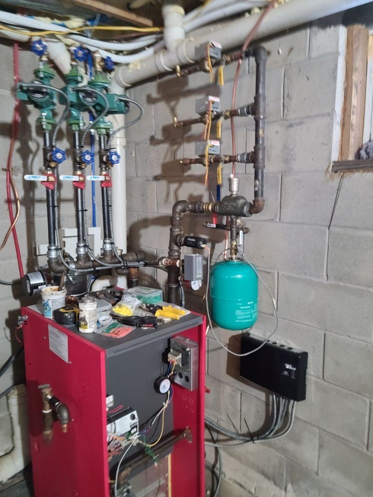 A red boiler is sitting in a basement next to a brick wall.