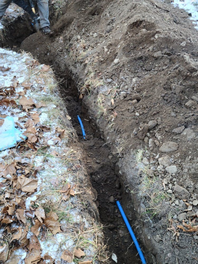 A man is digging a trench in the dirt with a blue pipe in it.