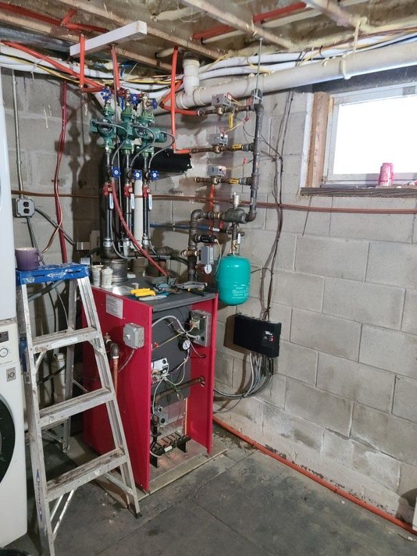 A red boiler is sitting in a basement next to a ladder.