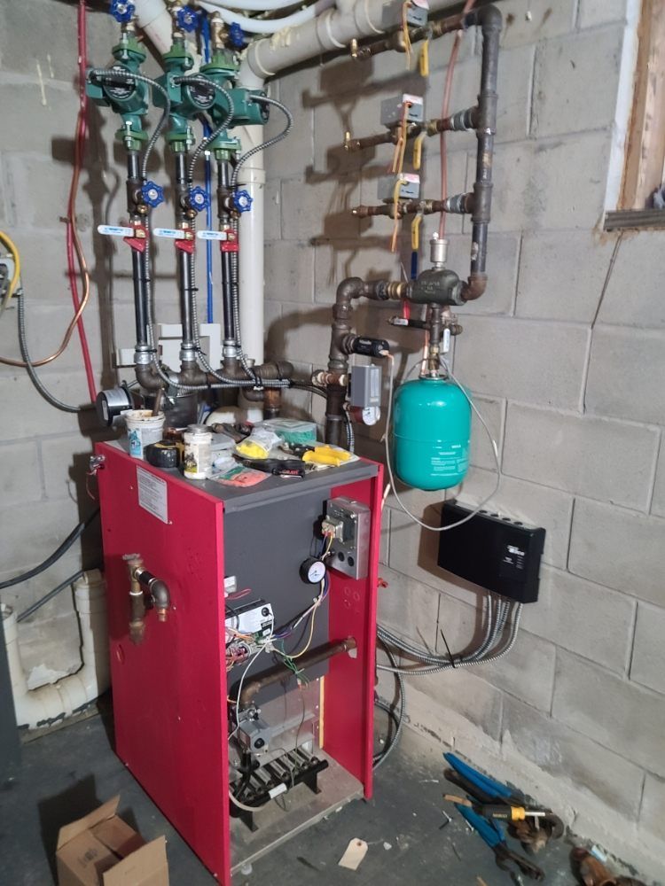 A red boiler is sitting in a basement next to a brick wall.