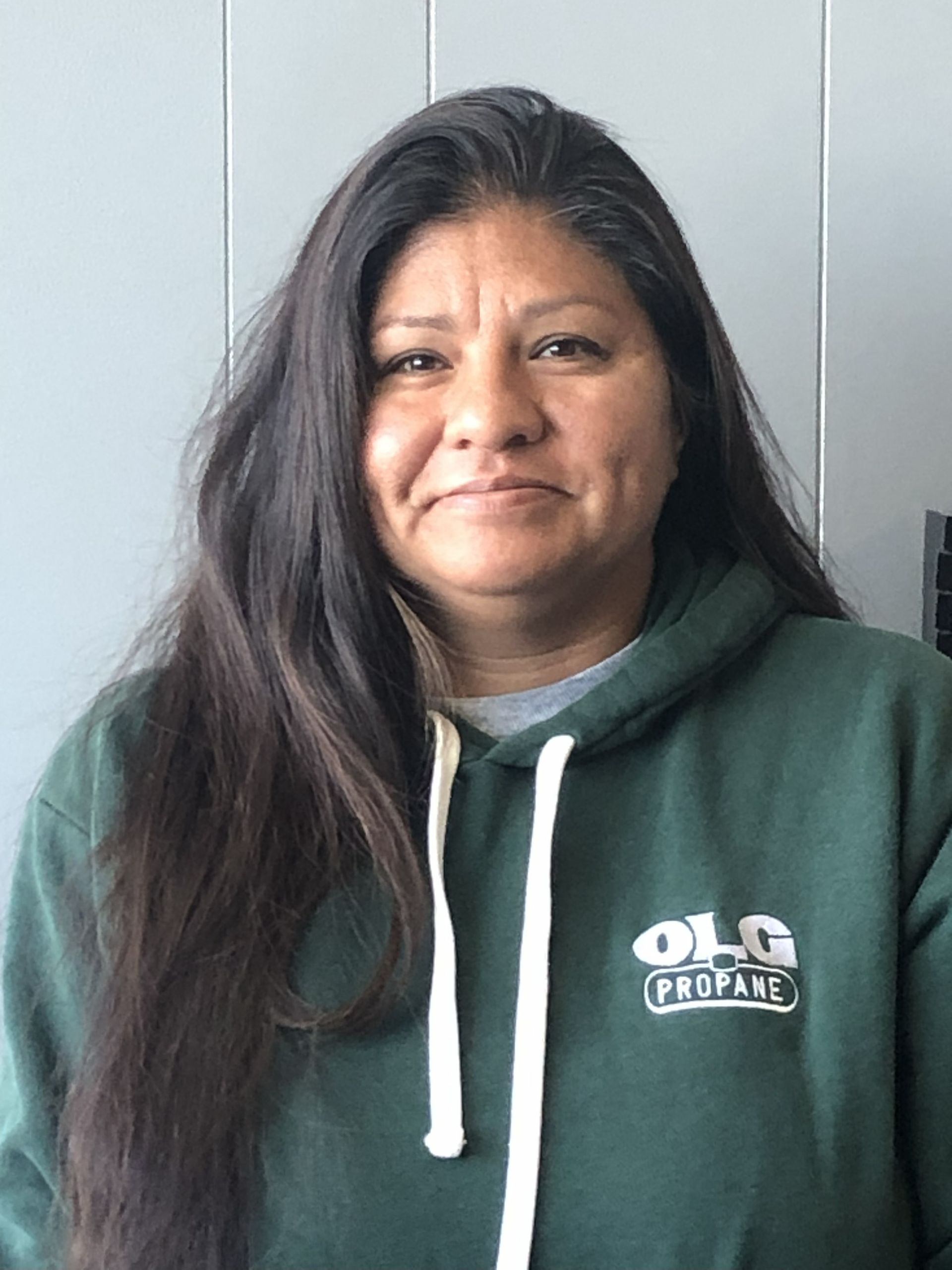 Woman with long dark hair, wearing a green hooded sweatshirt with the word