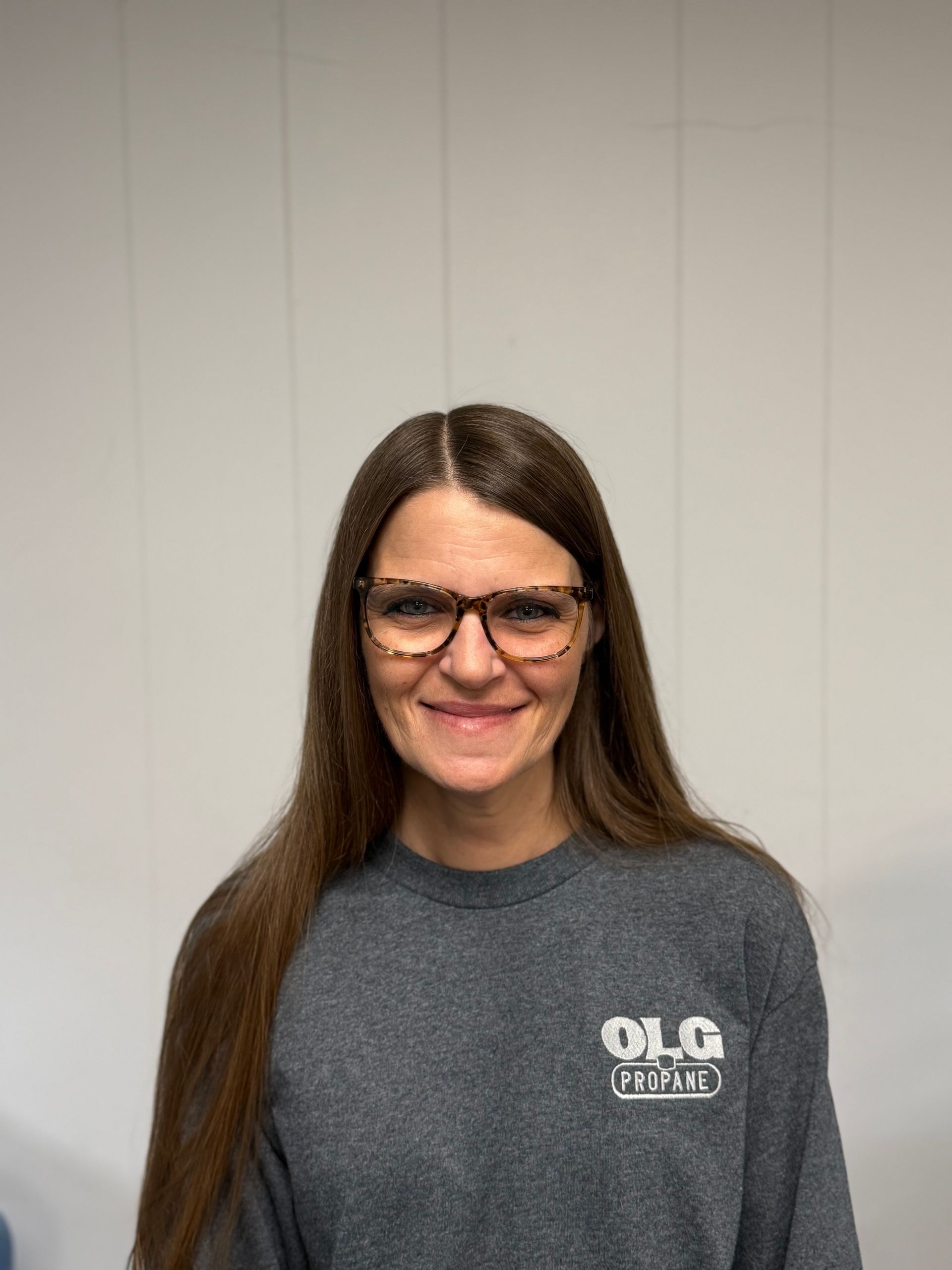 Woman with long brown hair wearing glasses and a gray sweatshirt smiles at the camera.