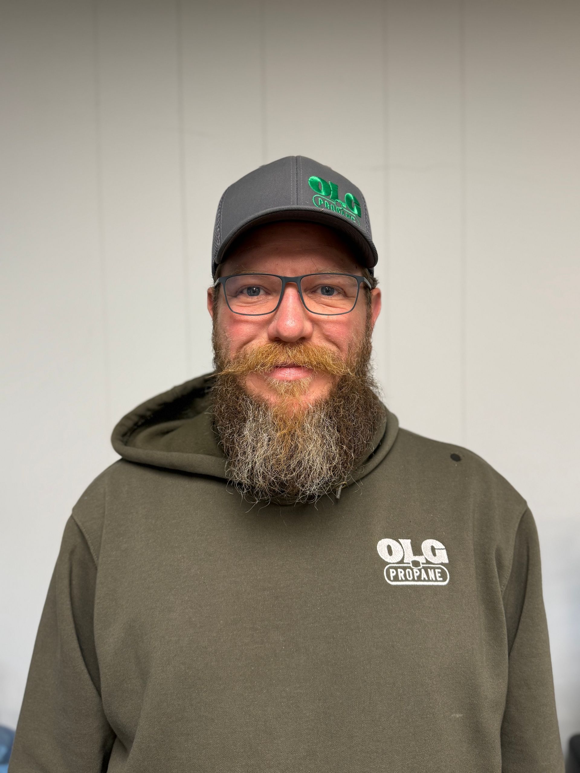 Man with beard wearing glasses and a cap, in a green hoodie.
