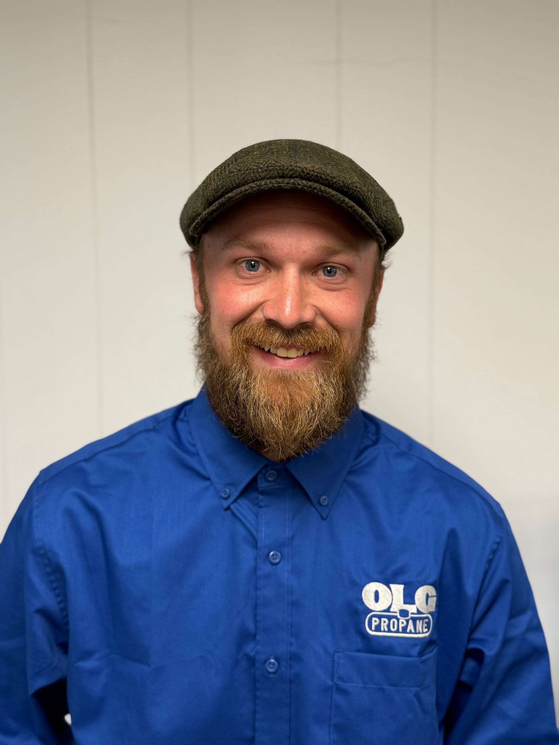 Man with beard wearing a newsboy cap and blue shirt with