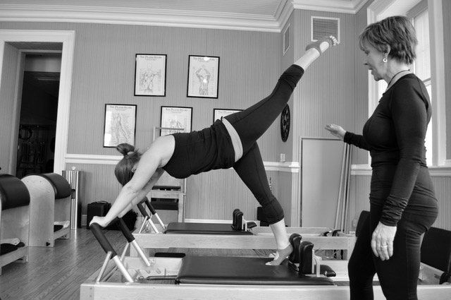 A woman is doing a Pilates pose on a pilates machine while a teacher watches