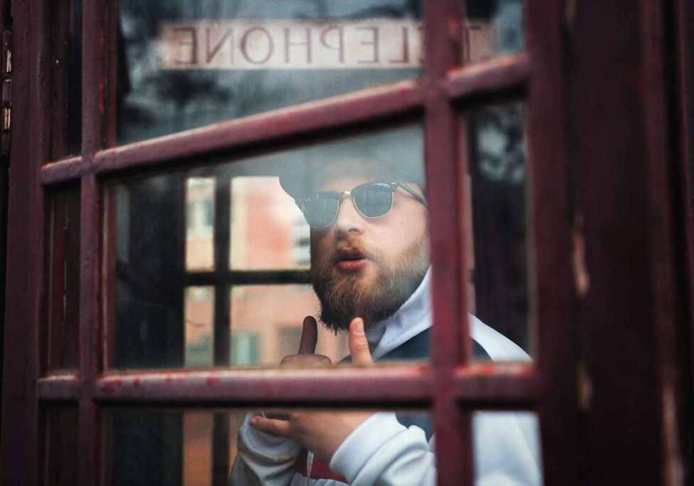 A man is talking on a cell phone in a phone booth.