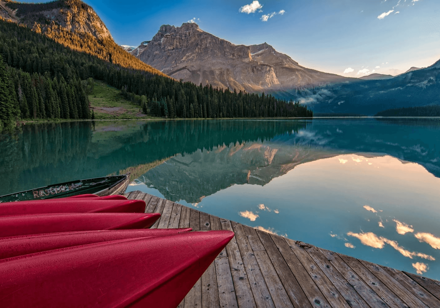 A couple of red kayaks are sitting on a dock next to a lake with mountains in the background.