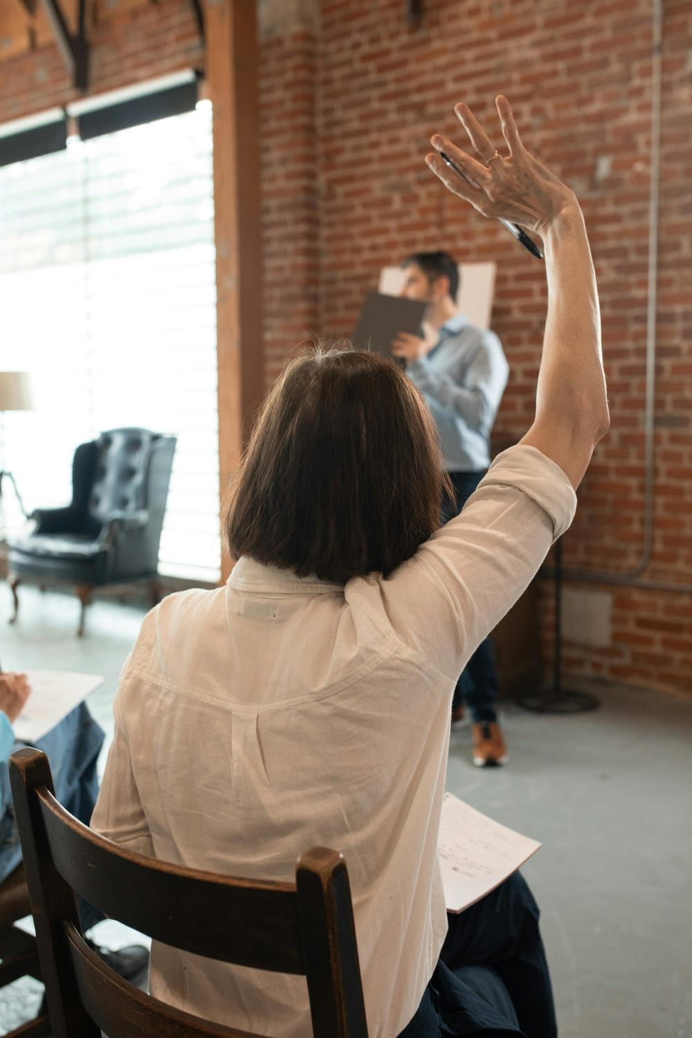 A woman is sitting in a chair with her hand up.