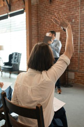 A woman is sitting in a chair with her hand up.