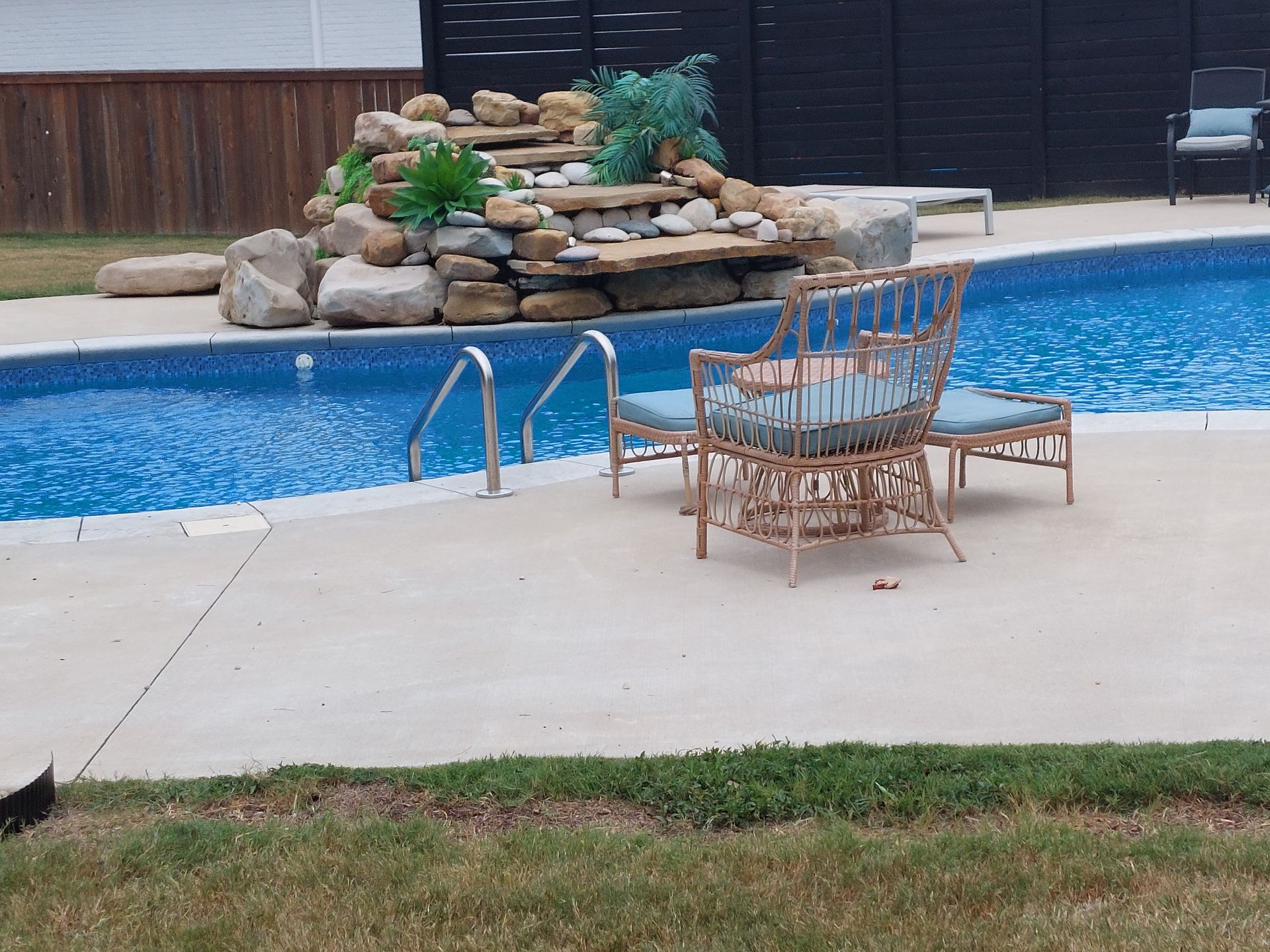 Swimming pool with waterfall feature, wicker furniture, and green lawn