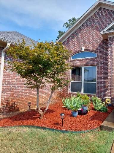 Red brick house with a tree and flower bed, mulched in red