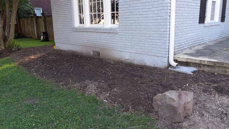 A house with gray brick siding and a mulch-covered flower bed