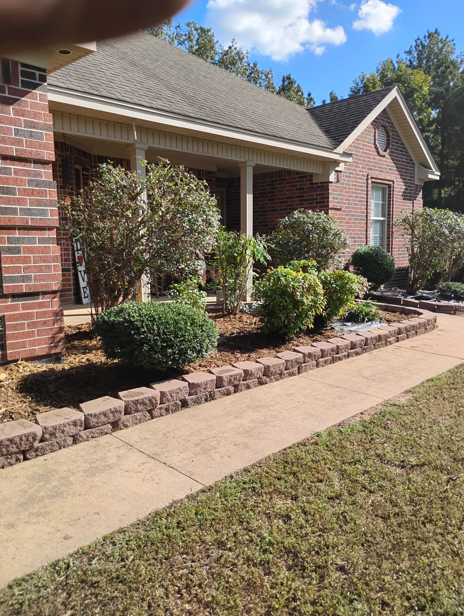 Red brick house with porch, flower bed bordered by dark bricks, walkway, blue sky