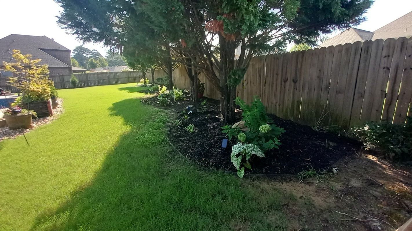 Lawn with a flower bed next to a wooden fence under trees