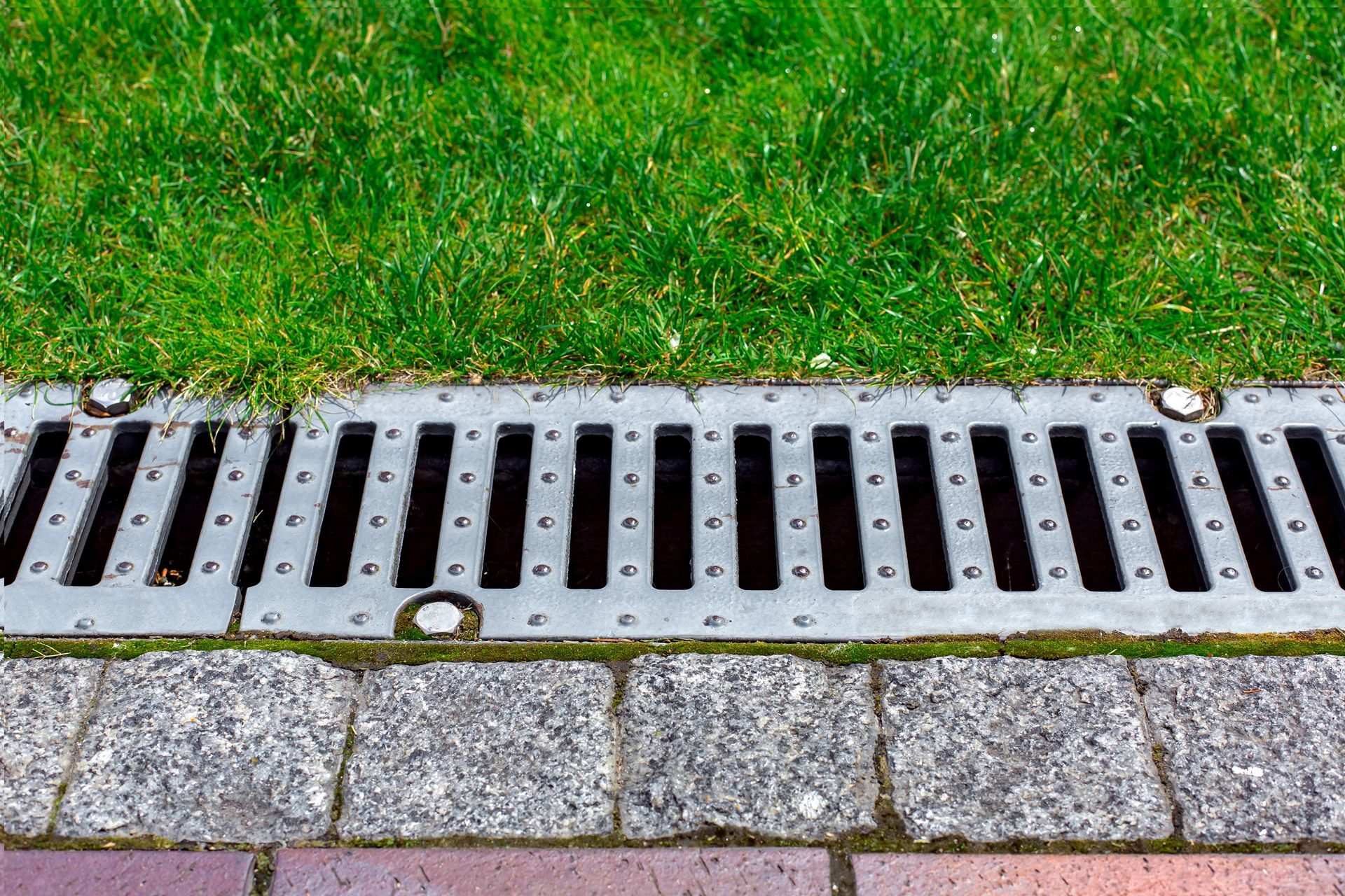 Drainage grate next to a grassy area and brick pathway