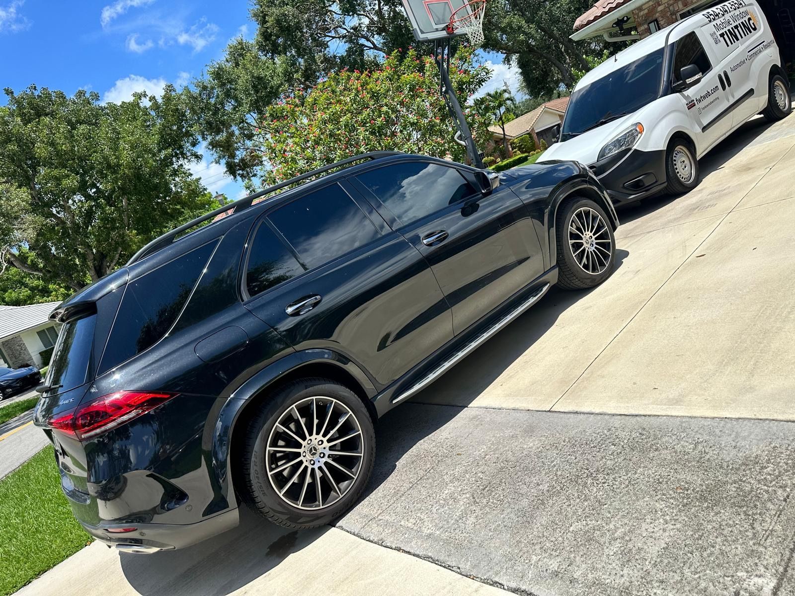 A black suv is parked in a driveway next to a white van.
